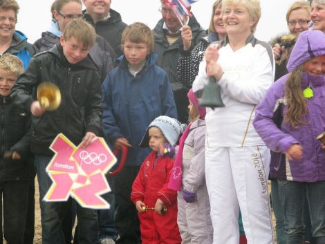 Belle Spence (in white) is joined by 40 others on Unst's Skaw beach and around the country to ring in the 2012 Olympic Games. Pic. Shetland Arts