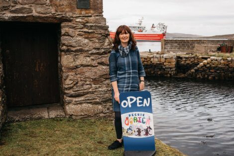 A woman standing next to a sign that says open.