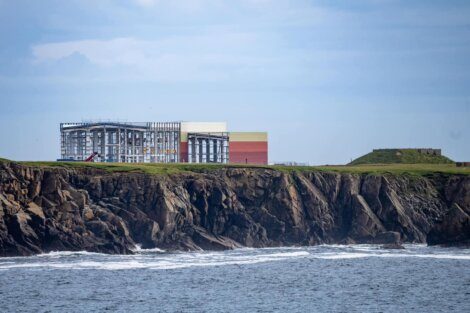Modern industrial building atop a rugged coastal cliff with the ocean in the foreground.
