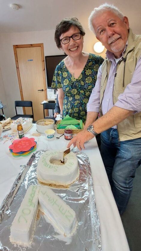 A man and a woman smiling while cutting a cake that reads 