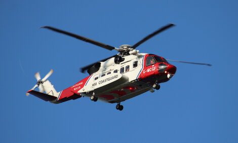 A red and white hm coastguard helicopter in flight against a clear blue sky.
