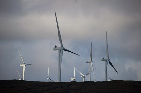 Several wind turbines on a hilly landscape under a cloudy sky.