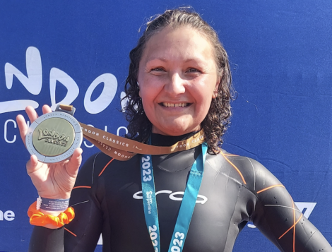 A smiling woman in a wetsuit proudly displaying her medal at a sporting event.