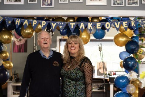 Two people smiling in a room decorated with blue and gold balloons and a banner reading 