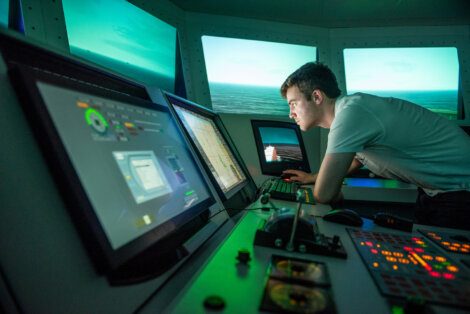 A man intently monitors navigation screens in a ship's bridge simulator.