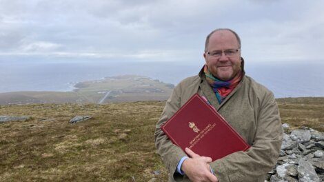 A man holding a red book on top of a mountain.
