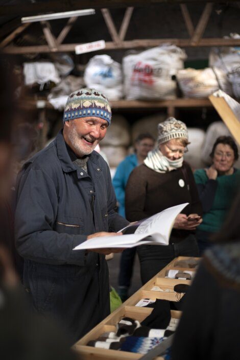 A man in a knit hat smiling while reading a document with attentive people surrounding him.