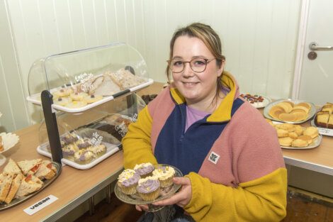 Woman presenting cupcakes at a bakery stand.