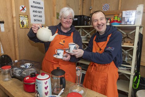 Two people in an orange apron holding tea cups.
