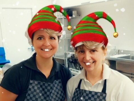 Two women wearing elf hats in a kitchen.