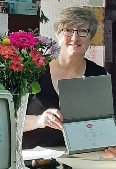 A woman holding a certificate and flowers in front of a computer.