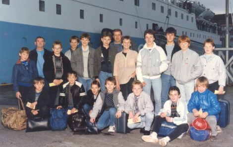 A group of boys posing in front of a large ship.