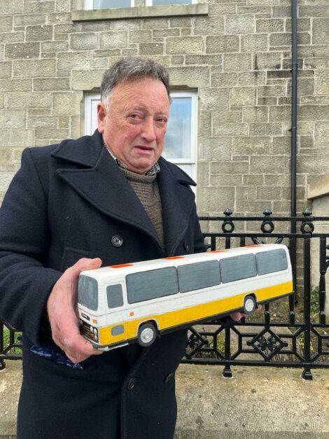 A man holding a toy bus in front of a building.