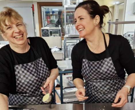 Two women smiling while preparing food in a kitchen.