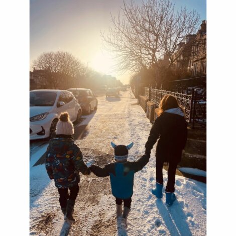 Two children holding hands walking down a snow covered street.