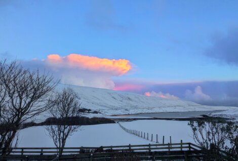 A pink cloud is seen over a snow covered hill.