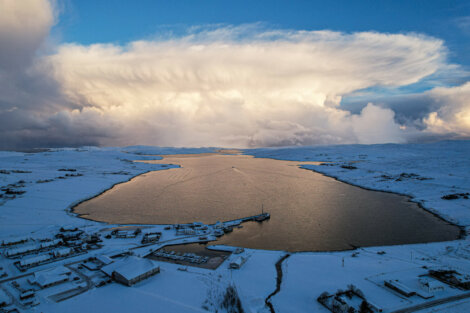 An aerial view of a snow covered lake with a cloud in the sky.
