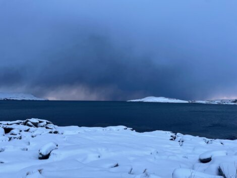 A stormy sky over a body of water with snow on the ground.