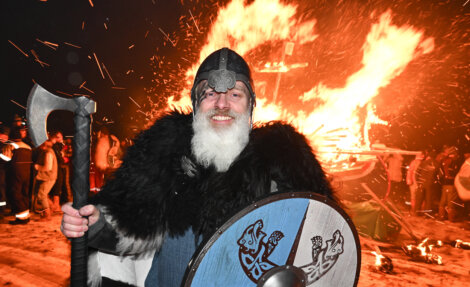 A man in viking costume standing in front of a bonfire.