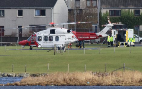 A white and red helicopter parked next to a body of water.