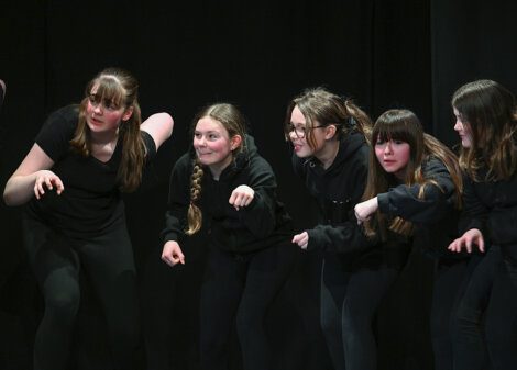 A group of young performers in black attire engaging in a theatrical act onstage.