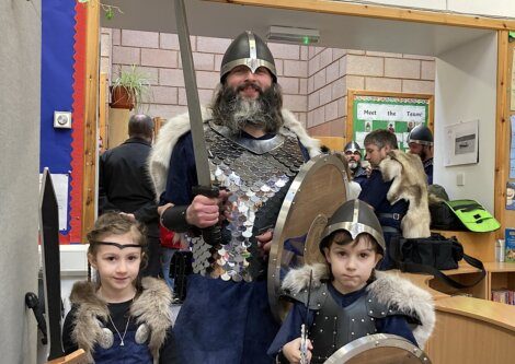 A person dressed as a viking warrior stands with two children, also in viking attire, possibly at a historical or cultural event.