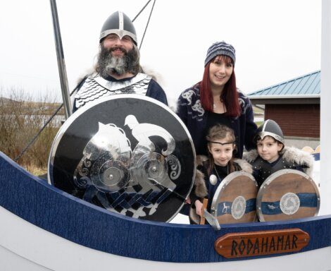 A family dressed in viking attire posing with a boat and shields at a themed event.
