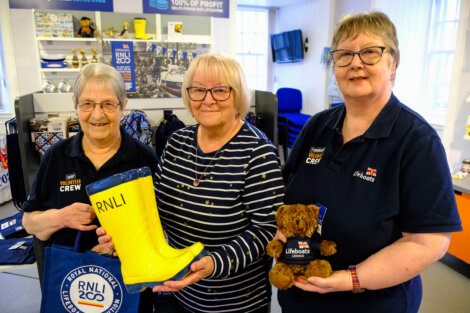 Three volunteers at a lifeboat charity shop posing with merchandise.