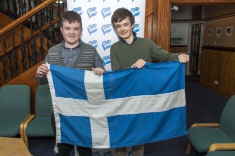 Two individuals holding the flag of scotland indoors.