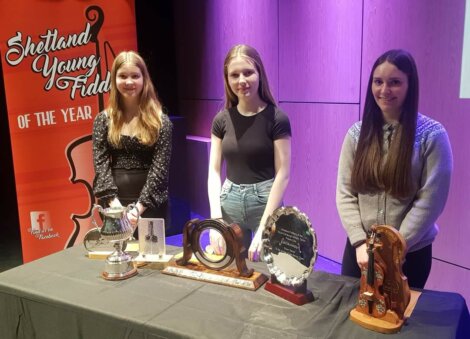 Three young women standing behind a table displaying trophies at the 