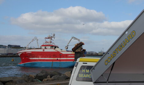 Red fishing vessel at sea with coastguard boat in the foreground.