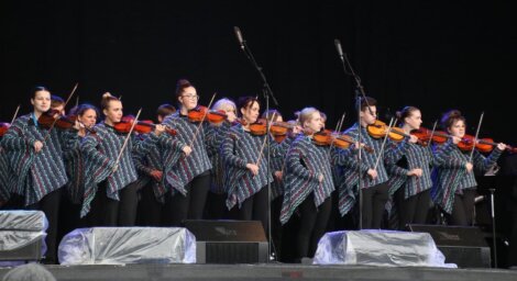 Group of violinists in matching outfits performing on stage.
